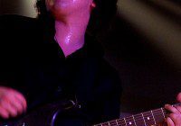 Musician passionately playing electric guitar under purple stage lights.