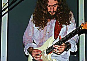 Man with long curly hair playing electric guitar on stage.